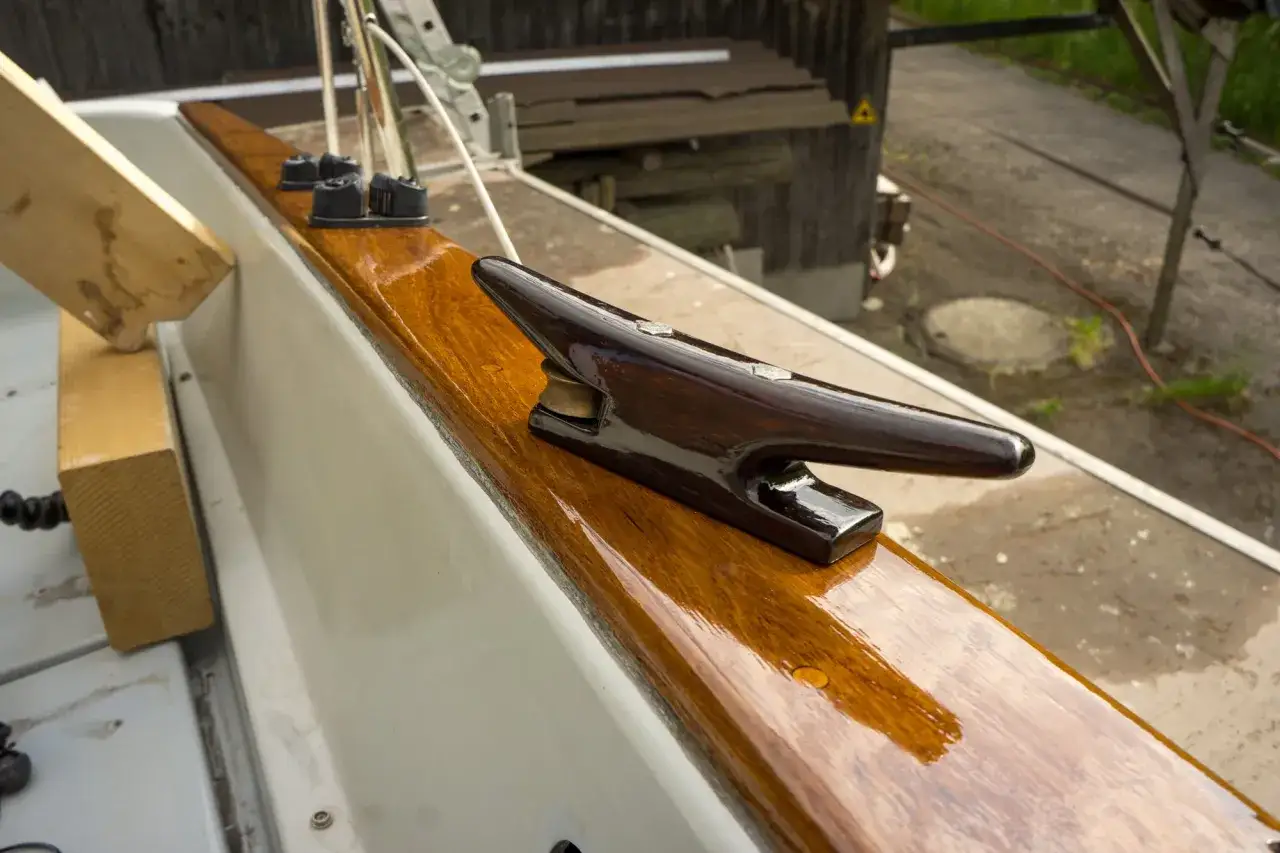 Glänzendes Holzdeck eines Bootes, frisch lackiert. Ein dunkler Klampen aus Holz sitzt auf dem glatten, polierten Holz.