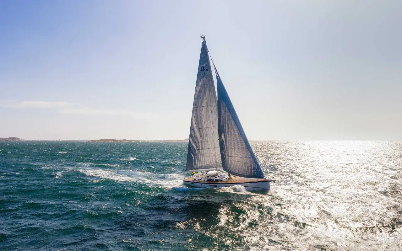 Eine Hallberg-Rassy 69 gleitet mit vollen Segeln über das glitzernde Meer.