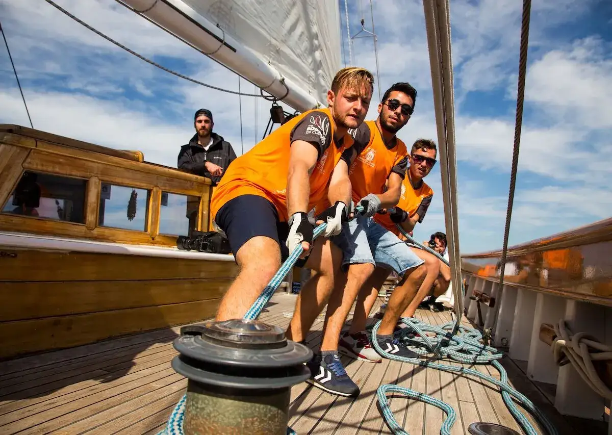 Crew members pulling ropes on La Vagabonde, a sailing adventure under a blue sky.