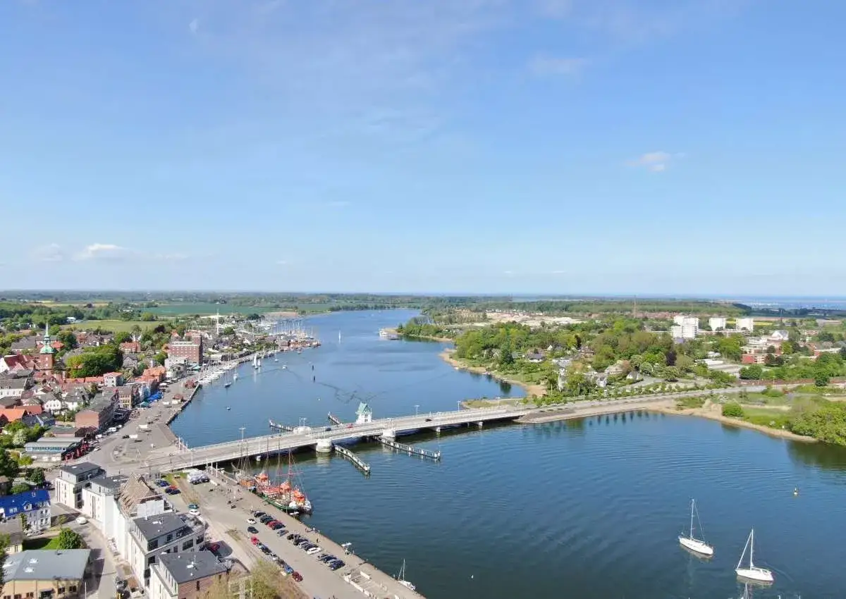 Blick über Kappeln an der Schlei mit Hafen, Brücke und Segelbooten im blauen Wasser.