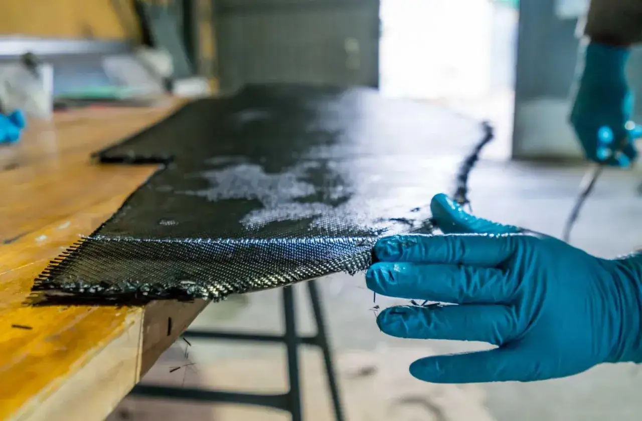Hand in blauer Handschuh bearbeitet Carbonfaser-Gewebe f&uuml;r den epoxidharz bootsbau.
