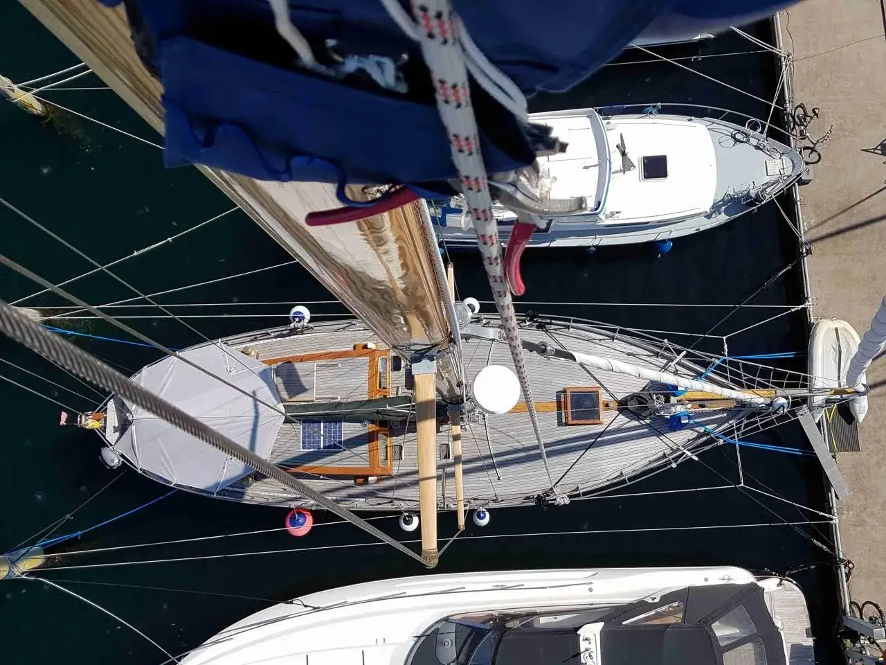 Blick von oben auf eine Rustler 36 mit Holzdeck und Solarpaneelen, daneben ein weiteres Segelboot und ein Motorboot.