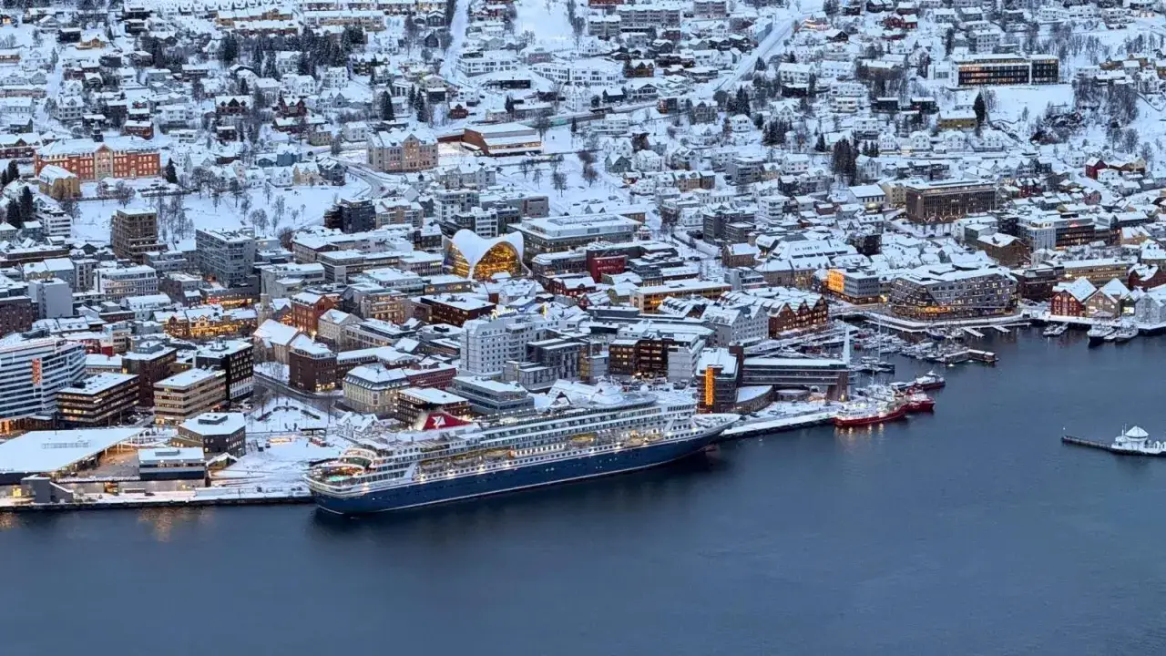 Schneebedeckte Stadt und ein gro&szlig;es Kreuzfahrtschiff im Troms&oslash; Hafen.