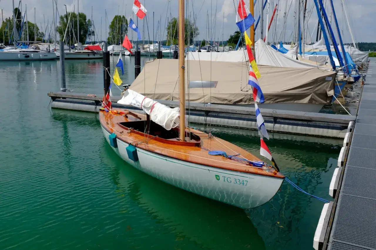 Eine elegante Holz-Segelyacht mit bunten Flaggen liegt im Hafen. TG 3347 ist auf dem Rumpf zu sehen. Die keller werft ist ein Ort der Ruhe.
