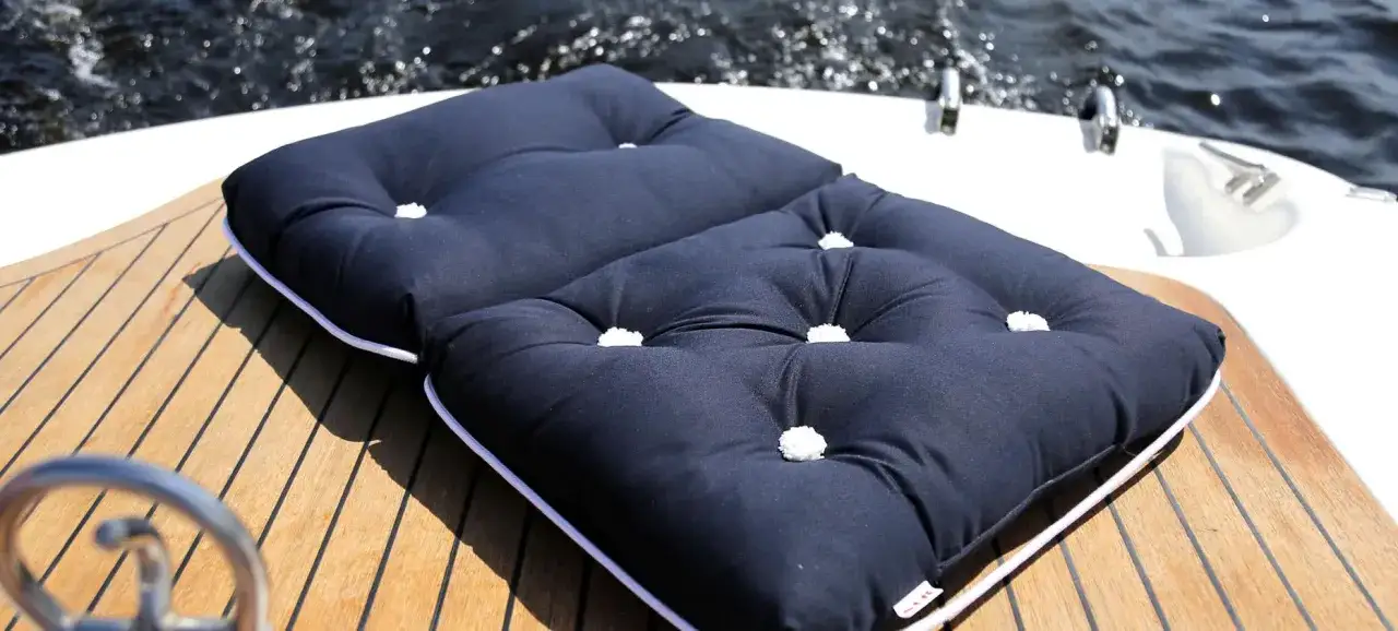 Dunkelblaues, gestepptes Kissen auf Teakdeck. Was ist Kapok? Dieses Kissen könnte mit Kapok gefüllt sein, einem leichten, wasserabweisenden Material.