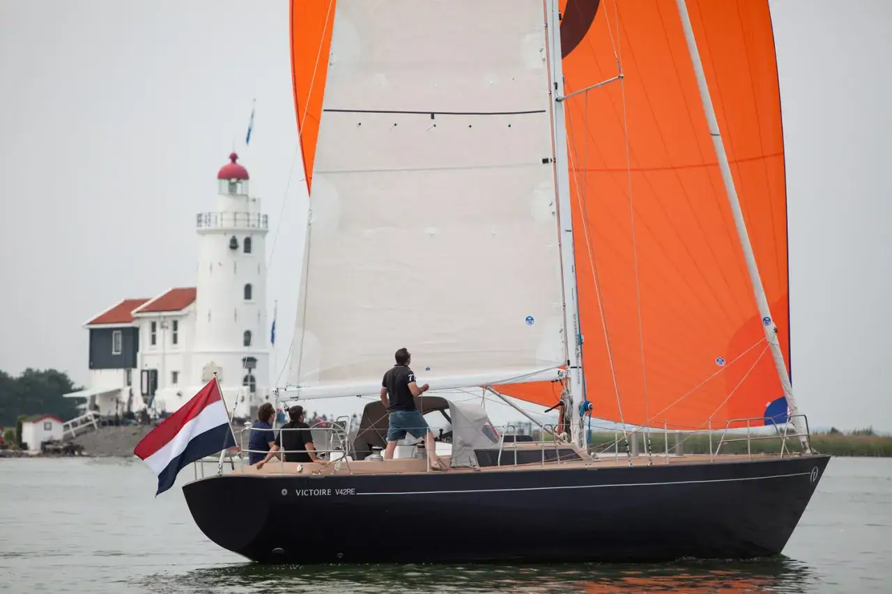 Segelboot mit orangefarbenen Segeln im Enkhuizen Hafen, im Hintergrund ein Leuchtturm.