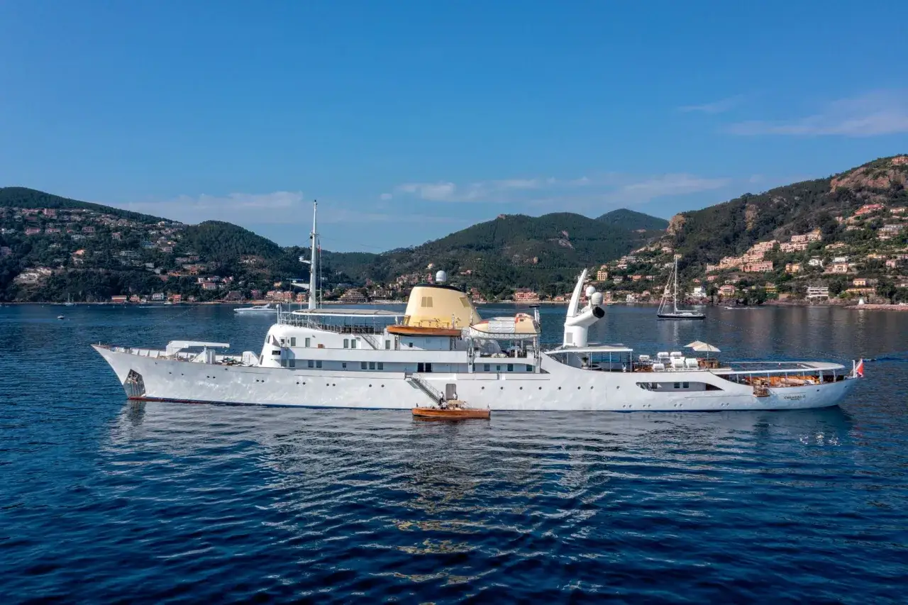 Die Christina O, ein luxuri&ouml;ses wei&szlig;es Schiff, ankert vor einer K&uuml;ste mit H&auml;usern, die sich an bewaldete H&uuml;gel schmiegen.