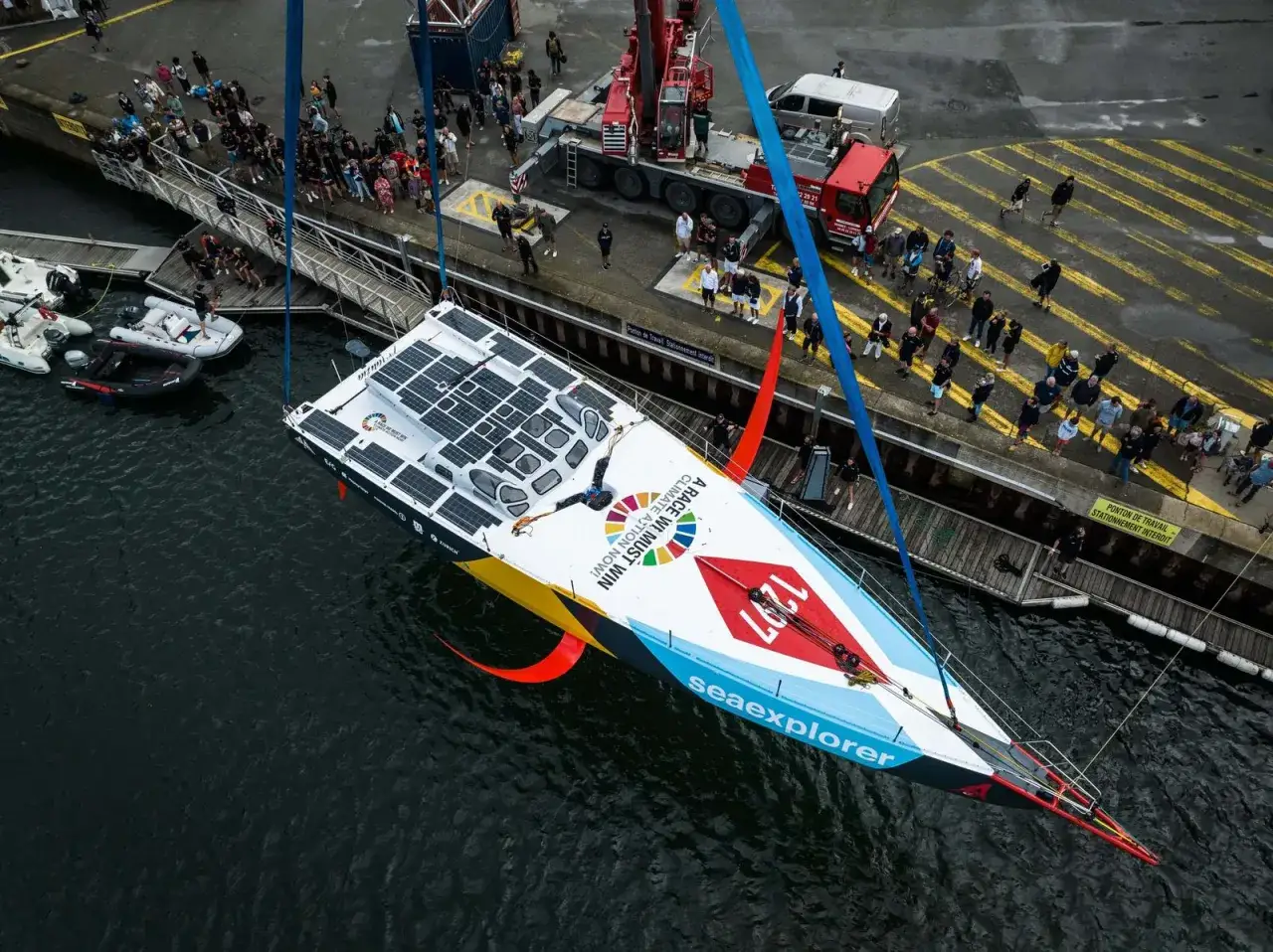 Malizia Ocean Race: Ein Segelboot mit Solarzellen wird gehoben. Eine Person liegt auf dem Deck.