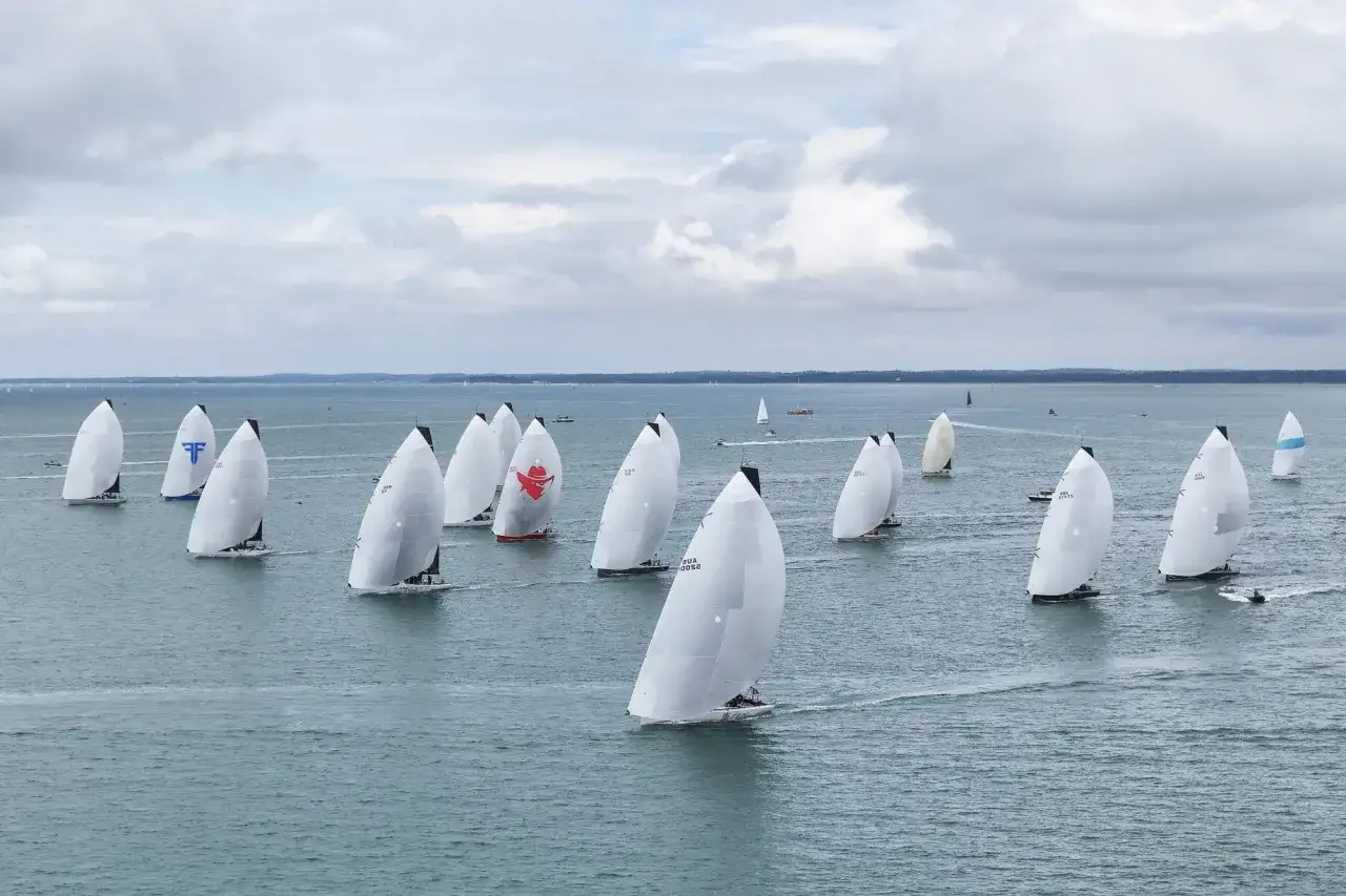 Segelboote kämpfen um die Admirals Cup Trophäe. Weiße Segel dominieren das Bild, während die Boote über das Meer gleiten.