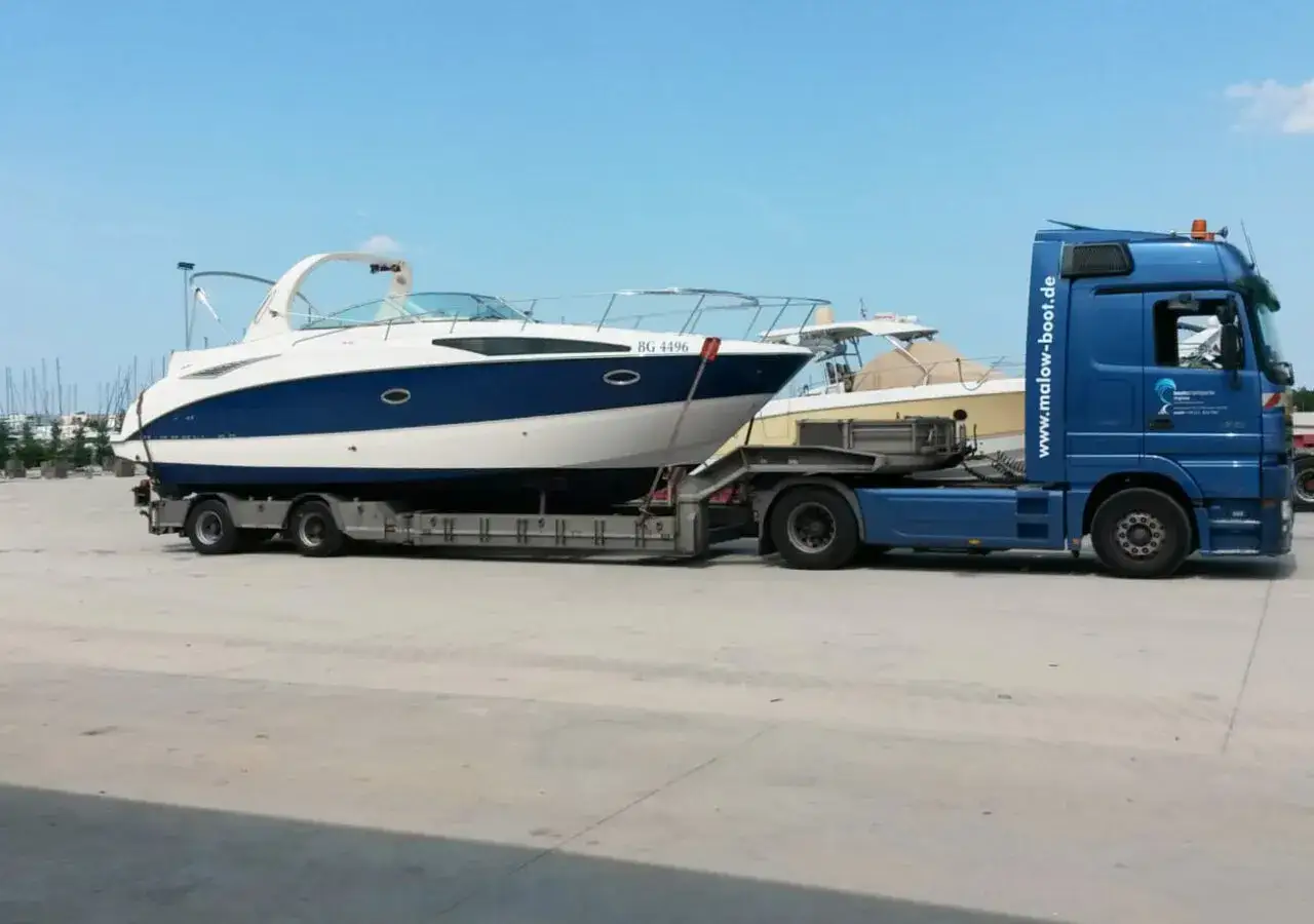 Blauer LKW transportiert ein wei&szlig;-blaues Boot auf einem Anh&auml;nger. Informieren Sie sich &uuml;ber bootstransport kosten.