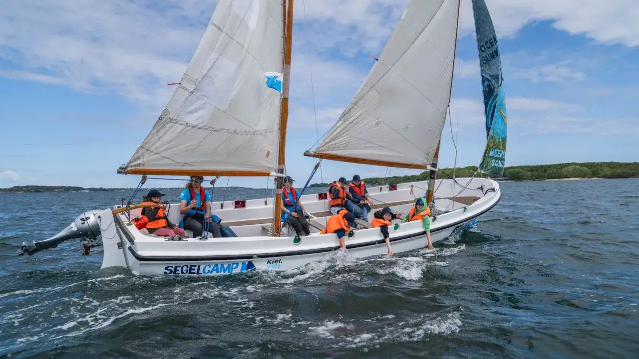Segelcamp Kiel: Kinder und Erwachsene genießen eine Bootsfahrt auf dem Wasser, einige mit Schwimmwesten.