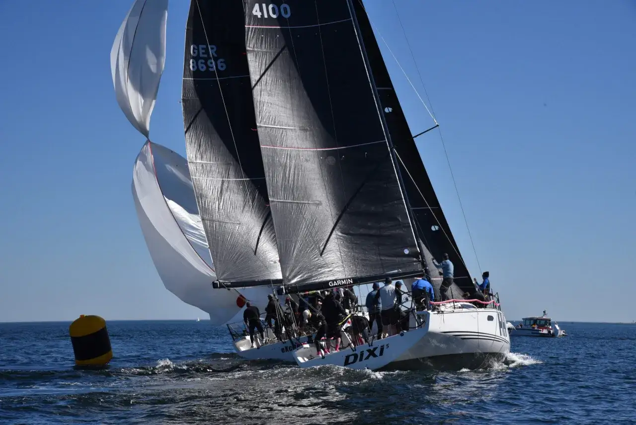 Segelregatta aktuell: Ein Segelboot mit schwarzen und weißen Segeln kämpft sich durch die Wellen. Die Crew ist aktiv, um die Segel optimal einzustellen.