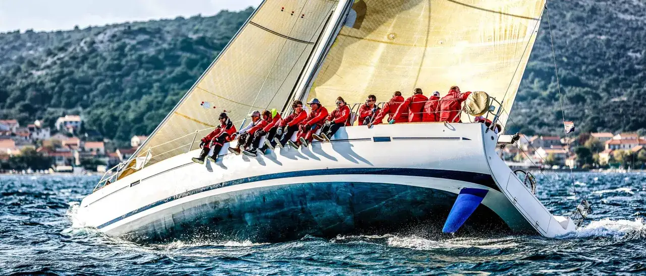 Segelboot mit Crew in roten Jacken, die auf der Reling sitzen. Tatjana Pokorny ist Teil dieses Teams, das über das Meer gleitet.