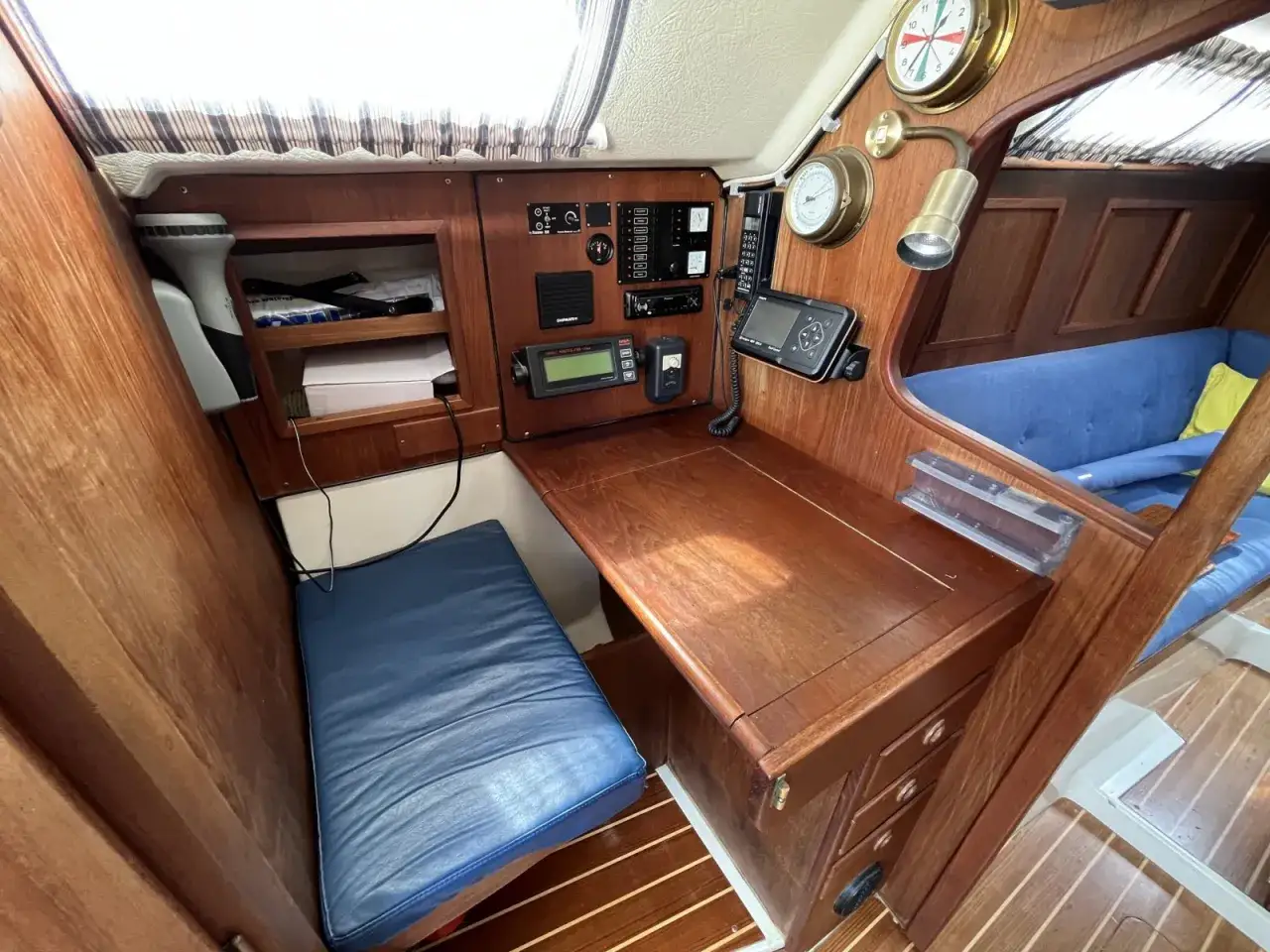 Gem&uuml;tliche Navigationsecke auf der Comfortina 32 mit Holztisch, blauem Sitzpolster und Navigationsinstrumenten.