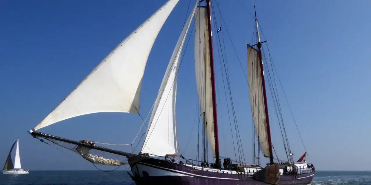 Segelschiff mit weißen Segeln vor blauem Himmel, auf dem Weg zum Harlingen Hafen.