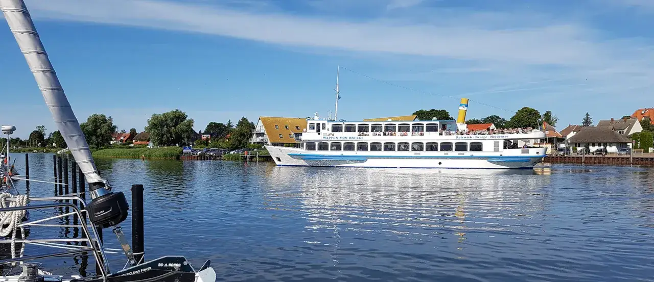 Ein Ausflugsschiff mit vielen Passagieren f&auml;hrt im breege hafen. Im Vordergrund ist ein Segelboot zu sehen.