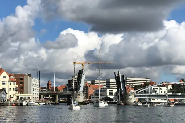 Sonderborg Hafen mit geöffneter Klappbrücke, Segelbooten und Gebäuden unter dramatischem Wolkenhimmel.