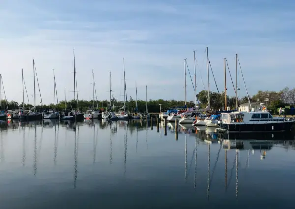 Segelboote und Motorboote liegen friedlich im Hafen Neuendorf, ihre Spiegelbilder tanzen auf dem ruhigen Wasser.