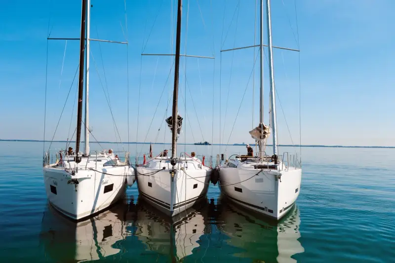 Drei weiße Segelyachten liegen nebeneinander im ruhigen Wasser. Ein Blick auf die elegante Bauweise, wie sie nur ein renommierter segelyacht hersteller hervorbringen kann.