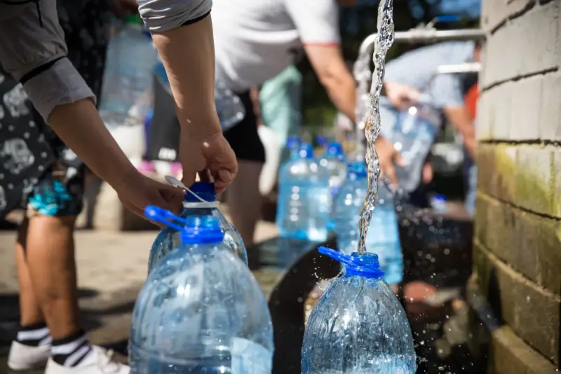 Menschen füllen Wasser in große Plastikflaschen. Die Frage, wie lange bleibt Wasser im Kanister frisch, ist hier relevant.